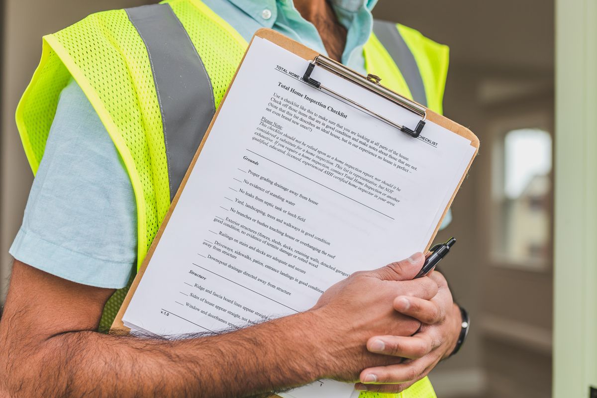 Inspector in a safety vest holding a clipboard with a printed home inspection checklist and a pen